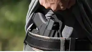 Man showing holstered gun inside waistband.