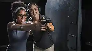 Woman showing another woman how to shoot a handgun at an indoor shooting range.